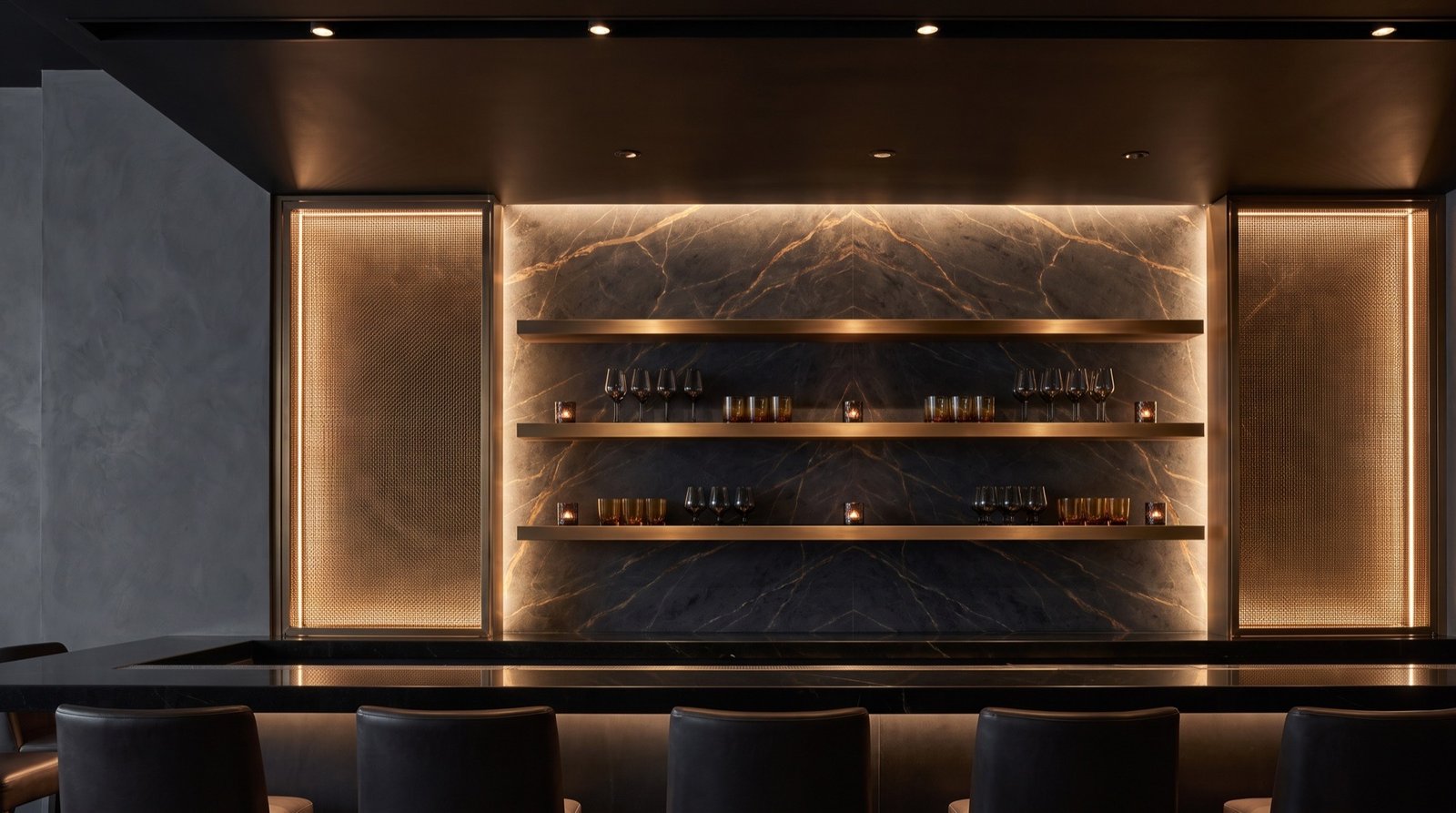 Bar after: bookmatched dark marble with backlit bronze mesh panels and floating bronze shelves