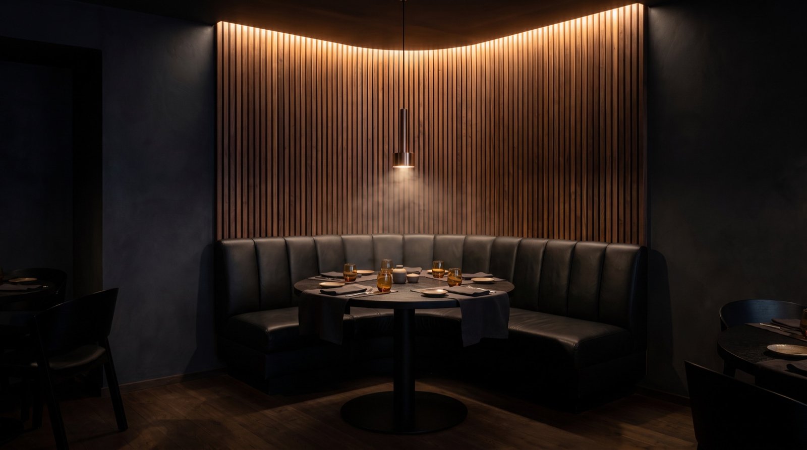 Corner banquette against the lit walnut slat wall with a single bronze pendant